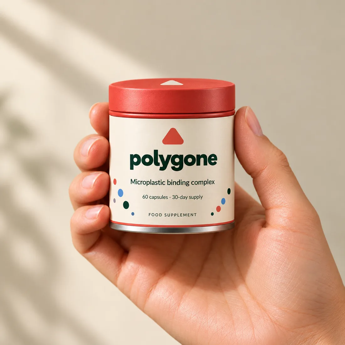 A hand holding the Polygone tin, with a coral lid and cream label reading Microplastic binding complex, against a warm cream wall