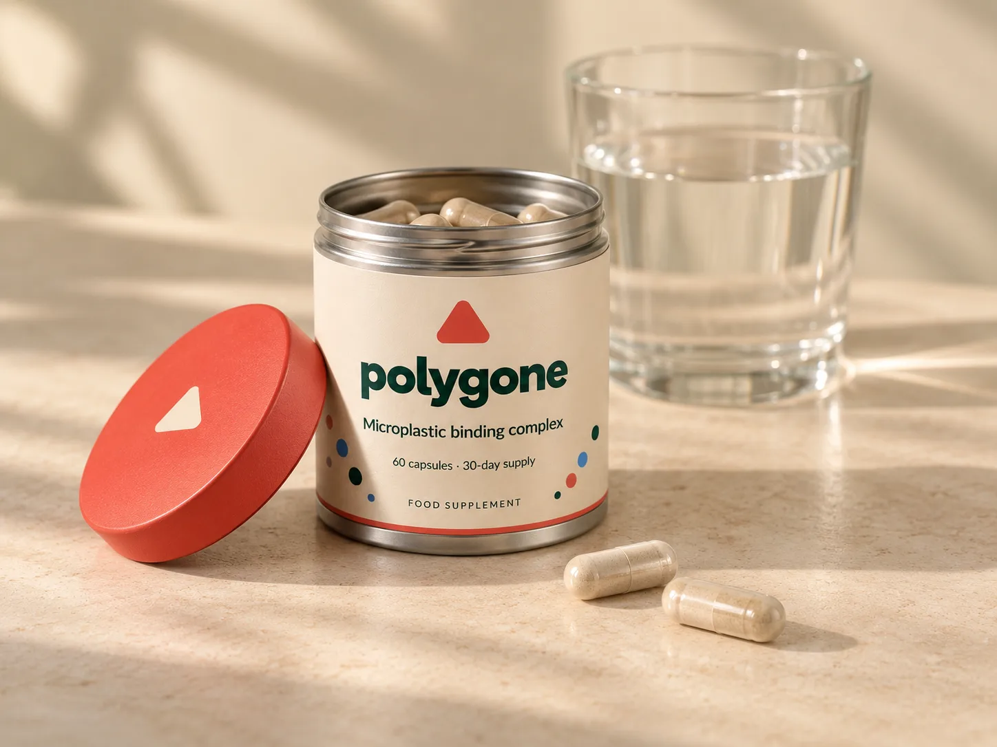 An open Polygone tin filled with capsules, its coral lid beside it, two capsules on the table and a glass of water behind